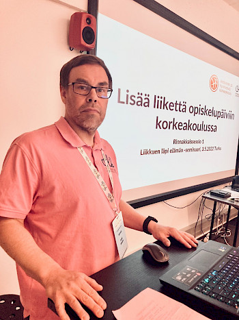 Kuvassa Jussi Ansala ja taustalla diaesityksen teksti "Lisää liikettä opiskelupäivään korkeakoulussa".